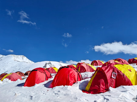 Bright red tents on a snowy mountain slope above the clouds, surrounded by majestic peaks and a deep blue sky, capturing the essence of high-altitude camping, adventure, and breathtaking landscapes.の写真素材