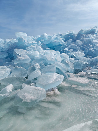 Bright blue ice chunks accumulate along the shoreline, shimmering under clear skies in a winter landscape.の写真素材
