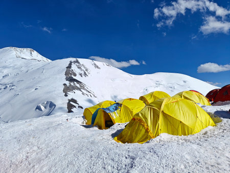 Brightly colored tents set up on a snowy plateau at Peak Lenin base camp, surrounded by majestic...