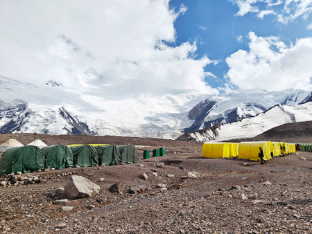 A colorful base camp with green and yellow tents set against the backdrop of snowy mountains and glaciers under a bright blue sky.の写真素材