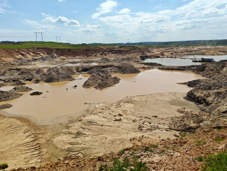 Large excavation area features muddy water pools and rocky terrain under a bright sky in a rural...