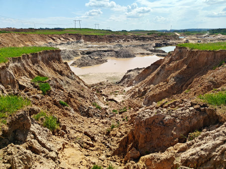 Large excavation area features muddy water pools and rocky terrain under a bright sky in a rural...