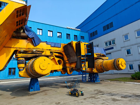 Industrial machinery stands outdoors near a blue building, highlighting its complex mechanical parts...