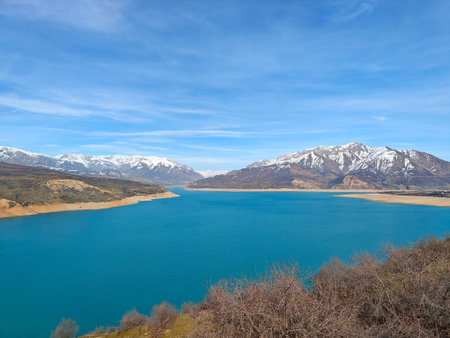 Tranquil blue lake reflects the surrounding snow-capped mountains under a clear sky, creating a serene natural landscapeの写真素材