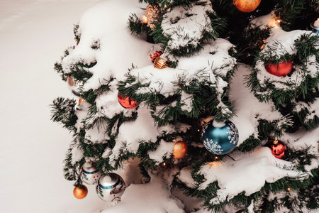 Snow-covered Christmas tree adorned with colorful ornaments, showcasing festive decorations and a winter wonderland atmosphereの写真素材
