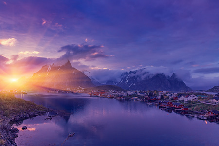 Reine on the Lofoten in northern Norway. The Typical Norwegian fishing village of Reine under midnight sun, blue sky, with the typical rorbu houses.  Mountain In Backgroundの写真素材