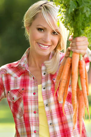A blonde farm girl holding carrotsの写真素材
