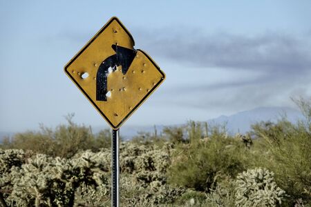 A street sign warning of a curve ahead is riddled with bullet holes.の写真素材