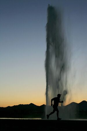 A silhouette of a man running by a fountain during sunset.の写真素材