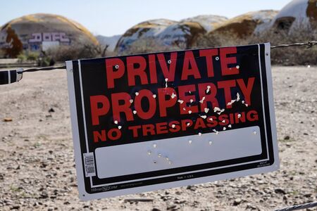 A private property no trespassing sign riddled with bullet holes.