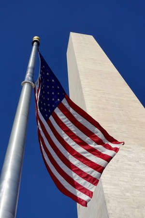 The American flag in front of the Washington Monument against a blue sky in Washington, D.C.の写真素材