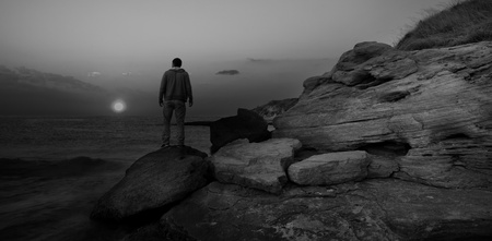 black and white sunrise seascape with alone man on the rocksの写真素材