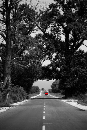 abstract black and white road with single red car in distance の写真素材