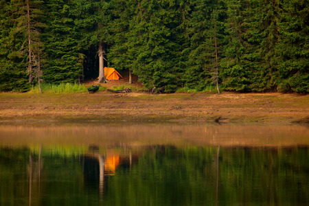 calm high mountain lake at sunset and single orange tent on the beachの写真素材