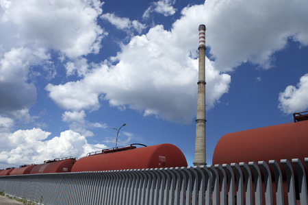 industrially manufactured landscape with vertical tall chimney and horizontal tank wagons lineの写真素材