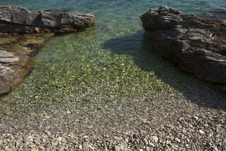 small beach with pebbles on entrance to crystal clear seaの写真素材