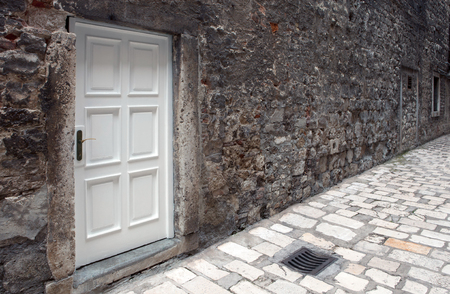 new white door on old dirty wall in narrow paved streetの写真素材