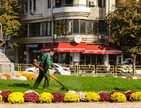 Man cutting the grass in the little park with grass and flowers in the center of Skopje のeditorial素材