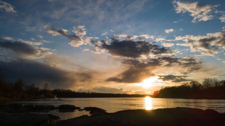 Beautiful sunset landscape by the river with a rocky shore.