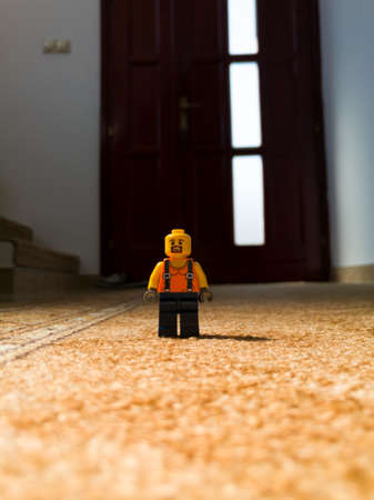 A Lego worker, a children's toy stands on the carpet in the hallway of the house against the front door in daylight during the day.のeditorial素材