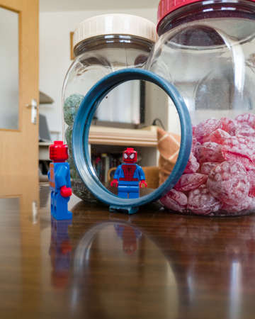 A reflection of a Lego children's toy, a superhero spiderman, in a mirror leaning against a jar of candy on the living room table.のeditorial素材