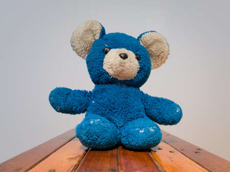 Insulated children's toy against a white background on a wooden chair, an old torn blue teddy bear from childhoodの写真素材