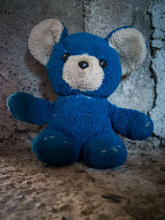 Insulated children's toy against a concrete wall, an old torn blue teddy bear from childhoodの写真素材