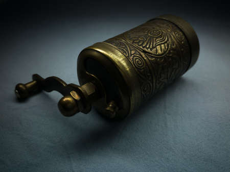 A small brass hand-held coffee grinder embossed on textiles against darkness. Traditional Turkish hand mill.の写真素材