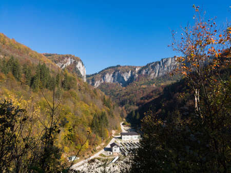 Scenic view of a mountain of steep rocky cliffs overgrown with forest above the building in autumn...