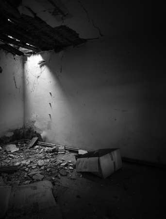 A corner in a messy spooky room with an opening in a rotten wooden ceiling and a mysterious cardboard box on the floor in an old abandoned house.の写真素材