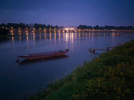 Quiet landscape of the Sava river with an anchored fishing boat near the wooden dock and Slavosnki Brod in the background during cloudy duskの写真素材