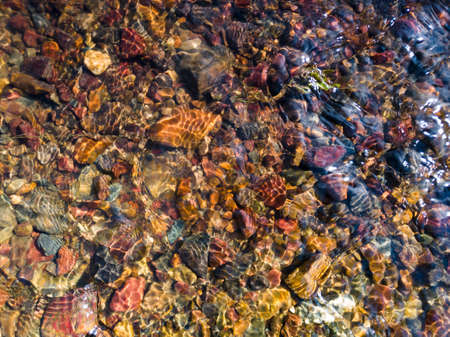 Detail from the creek, the shallow water flows over the colorful gravel and makes a pattern of...