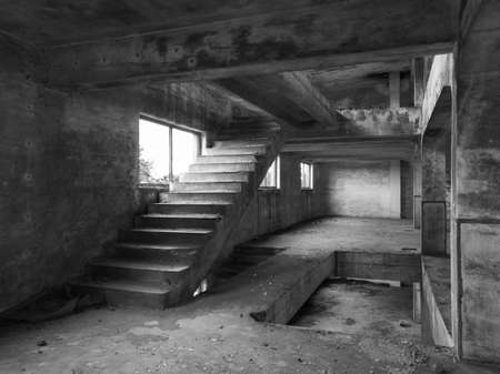 Staircase between floors in an empty messy industrial warehouse, urban exploration of the interior of an abandoned building, with broken windows and large pillars, concrete structureの写真素材