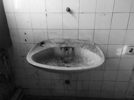 Detail from messy interior of abandoned building. Empty room with old dirty sink, cobweb and wall tiles.の写真素材