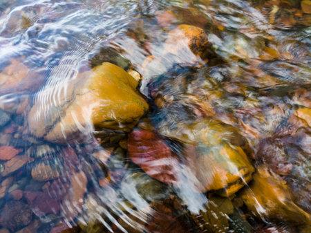Wavy surface of water on shallow rapid stream with colorful gravel at bottom, running water in creekの写真素材