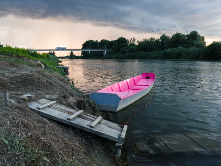 Storm arcus shaft and cumulonimbus cloud with heavy rain or summer shower, severe weather and sun glow behind rain. Landscape with Sava river with moored boat next to wooden dock and bridge.の写真素材