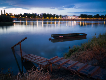 Cloud overcast evening during blue hour. Landscape with Sava river, cityscape, moored fishing boat near wooden dock in Bosanski Brod, Bosnia and Herzegovinaの写真素材