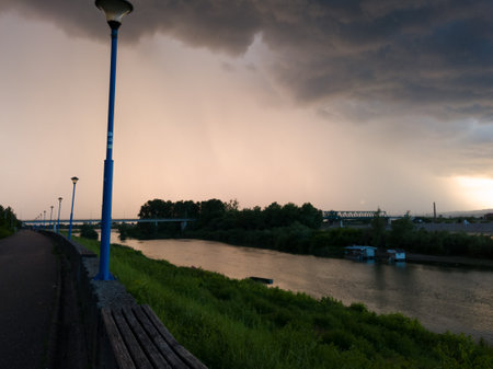 Storm cumulonimbus cloud with heavy rain or summer shower, severe weather and sun glow behind rain. Landscape with Sava river and promenade in Bosanski Brod, Bosnia and Herzegovinaの写真素材