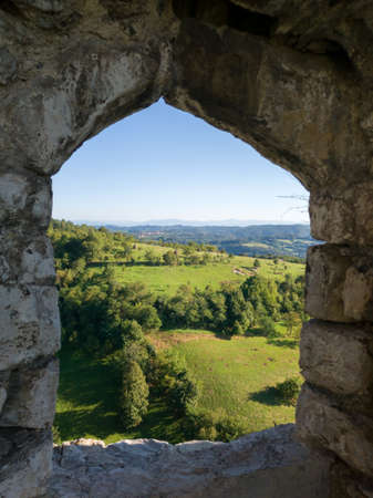 Panoramic hilly landscape of Srebrenik village with forests and meadows viewed through stone window of medieval ottoman fortress Srebrenikの写真素材