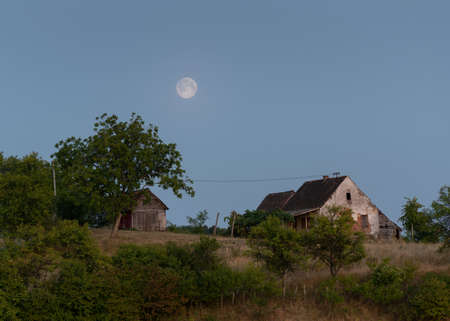 Abandoned farmhouse and shed in the countryside and full moon risingの写真素材
