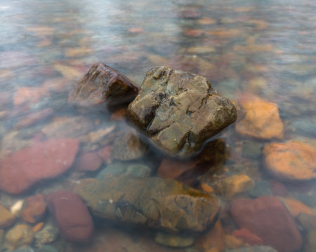 Two wet stones in shallow water and colorful underwater stones in long exposureの写真素材