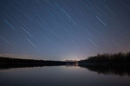 Star trails at night sky above silhouettes of forest and mountainの写真素材