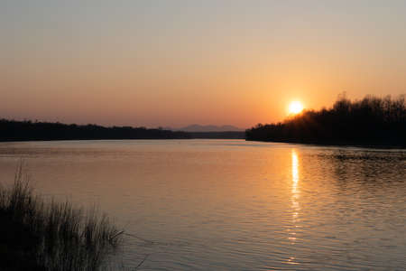 Landscape of river and mountantain before sunset, rippling water and distant mountain in haze with sun on clear sky, calming fair weather in natureの写真素材