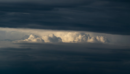 Bright sunlit cloud visible through opening in dark cloud, abstract landscape