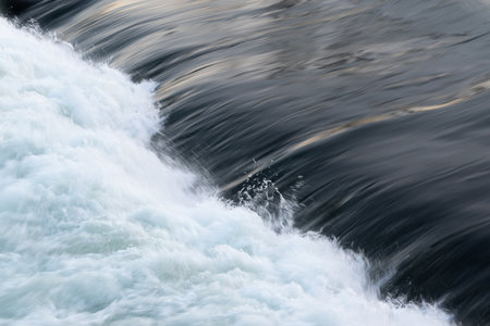Rapid water flow over barriere, river overflow over dam close up with splash and foam, abstract...