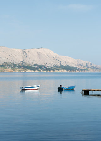 Two boats moored at sea near dock, mountainous island in backgroundの写真素材