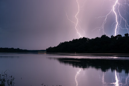 Beautiful lightning during thunderstorm at dusk over Sava river, lightning reflection on water surfaceの写真素材