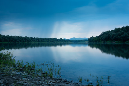 Landscape with river Sava and mountain in background during heavy rainfall, gloomy clouds reflecting in water surfaceの写真素材