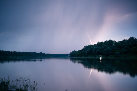 Beautiful lightning during thunderstorm at dusk over Sava river, lightning reflection on water surfaceの写真素材