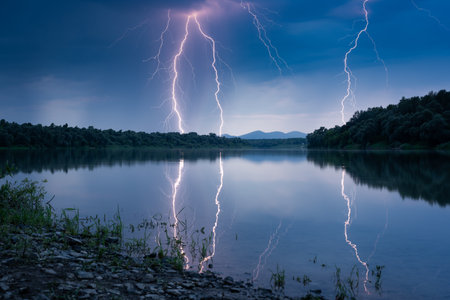 Beautiful lightning during thunderstorm at dusk over Sava river, lightning reflection on water surfaceの写真素材